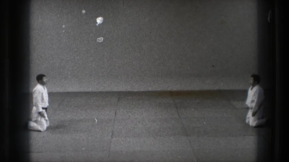 Wide 1971 Tokyo frame of two karate practitioners kneeling apart in a sparse indoor dojo.