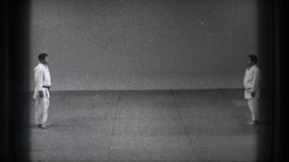 1971 Tokyo 8mm frame showing two karate practitioners standing face to face in a plain dojo.