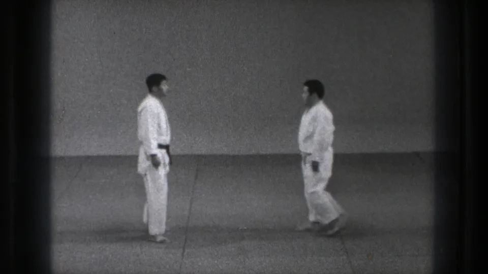 Near the end of the Tokyo 1971 clip, two adult practitioners in white gi stand close and face each other on the dojo mat.