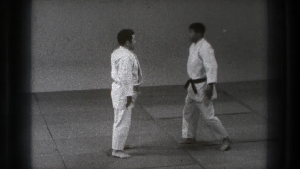 Two adult men in white gi face one another on a mat in a simple Tokyo dojo setting from 1971.