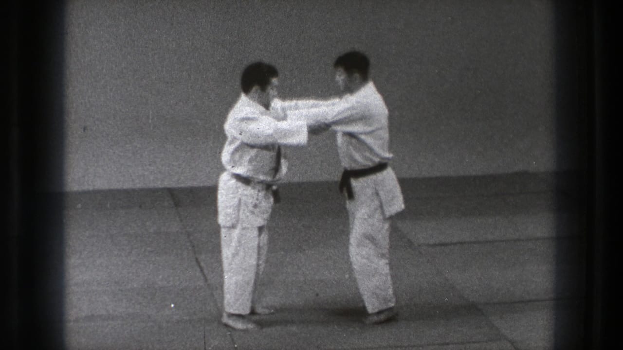 Two men in white gi face each other on an indoor mat.