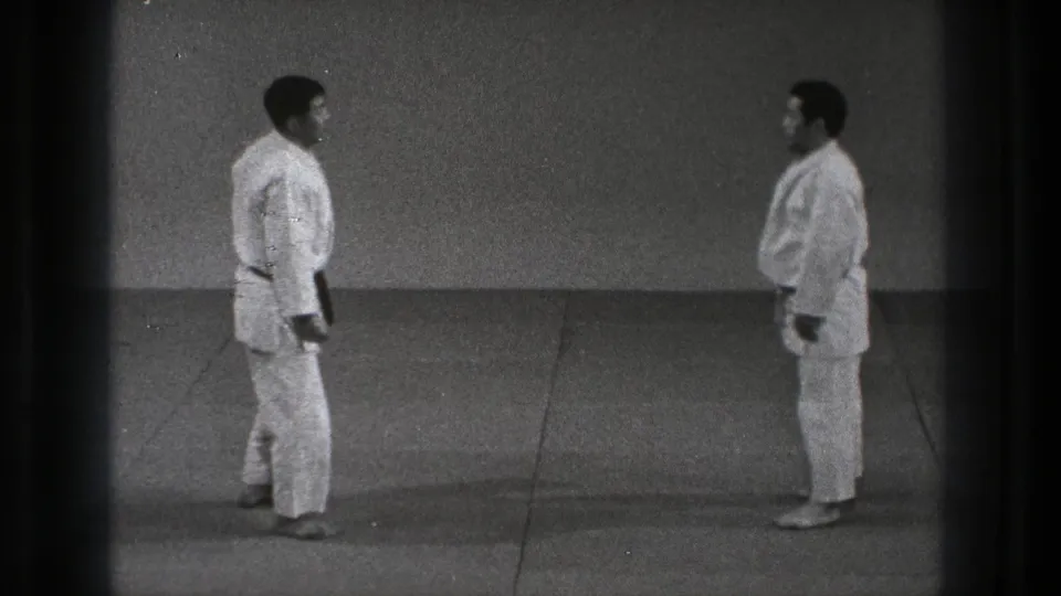 Two adult martial arts practitioners stand face to face in white gi during a 1971 Tokyo training moment.