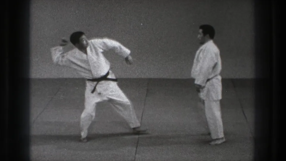 A 1971 Tokyo martial arts demonstration shows one man moving through a wide technique while his partner watches.