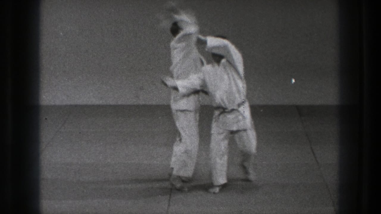 Two men in white gi begin a martial arts throw on a mat.