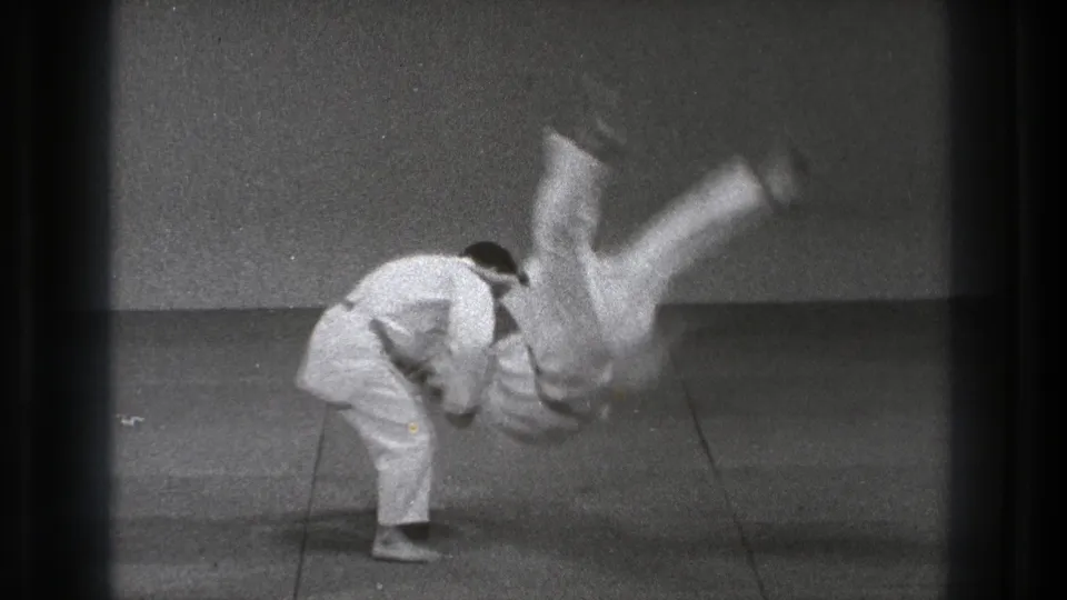 In the 1971 Tokyo practice sequence, one man bends forward while throwing his partner, whose legs are raised above the mat.