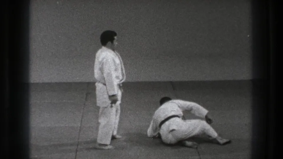 At the end of the Tokyo 1971 martial arts sequence, one practitioner stands as the other recovers on the mat after the throw.