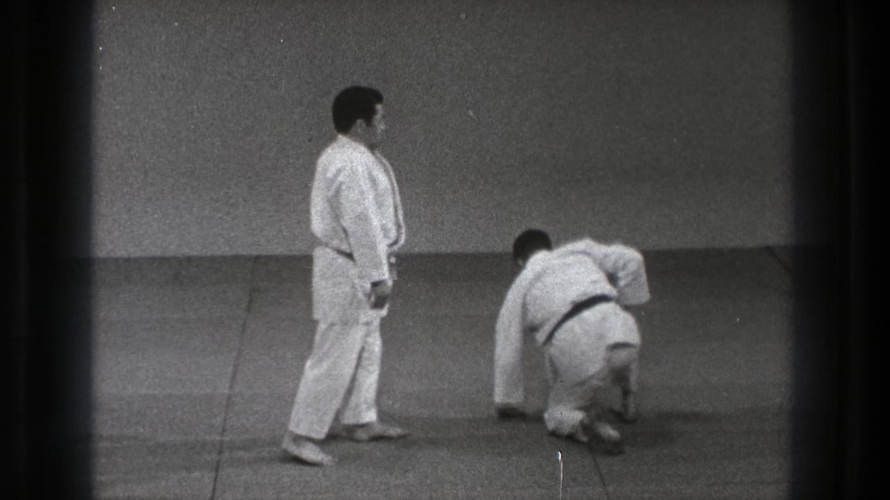 In the supplied 1971 Tokyo clip, two adult men in white gi practice on an indoor mat as one crouches and the other stands nearby.