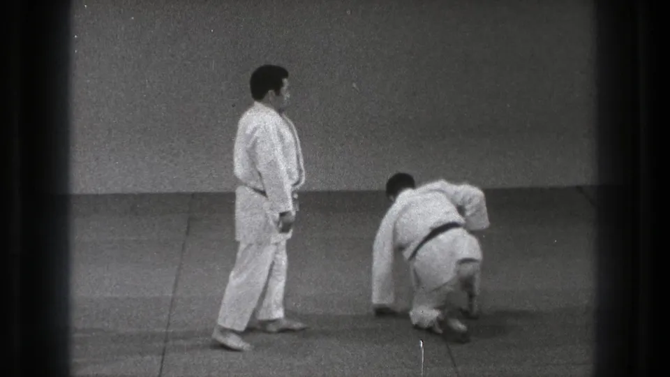 In the supplied 1971 Tokyo clip, two adult men in white gi practice on an indoor mat as one crouches and the other stands nearby.
