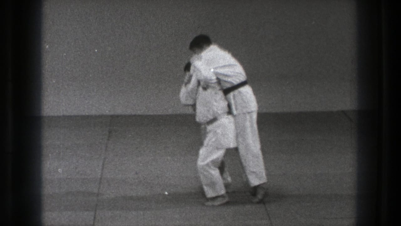 In 1971 Tokyo footage, two adult men in white martial arts uniforms grip each other during a dojo throw drill.