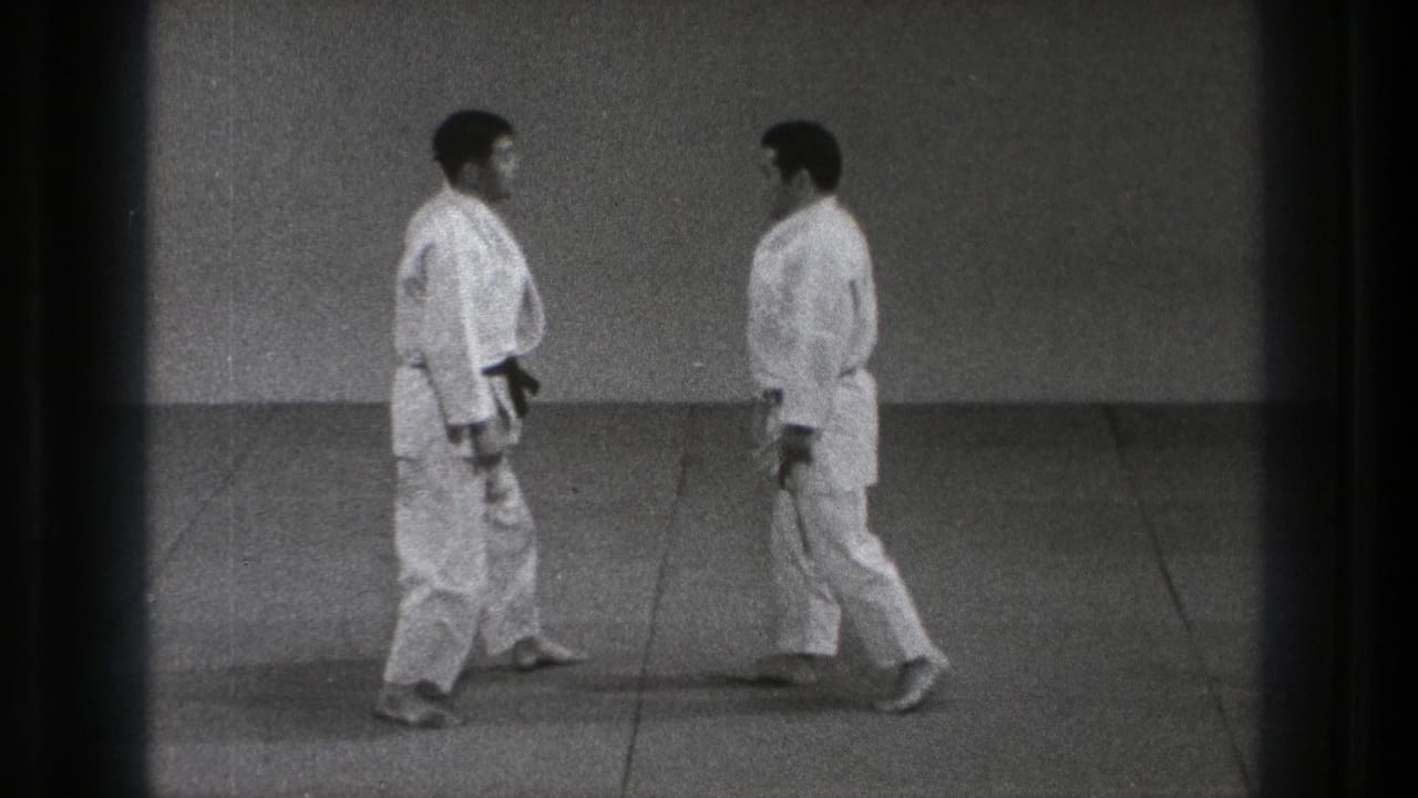 Two men in karate gi walk toward each other across a matted floor.