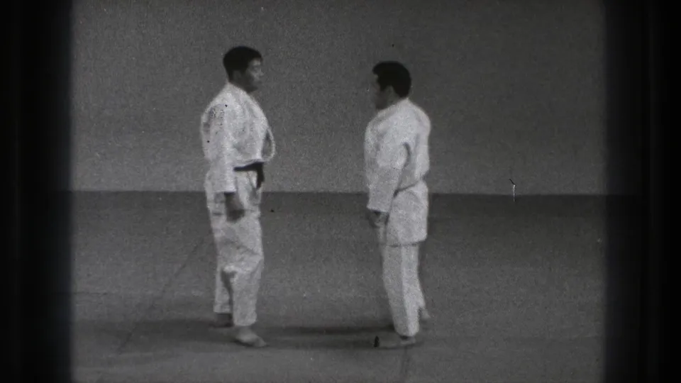 1971 Tokyo 8mm frame of two adult men in karate uniforms facing each other in a simple indoor training space.