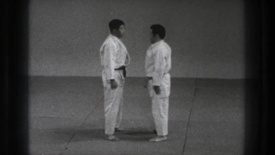 1971 Tokyo 8mm frame showing two adult karate practitioners standing close together on mats in a formal face-to-face position.