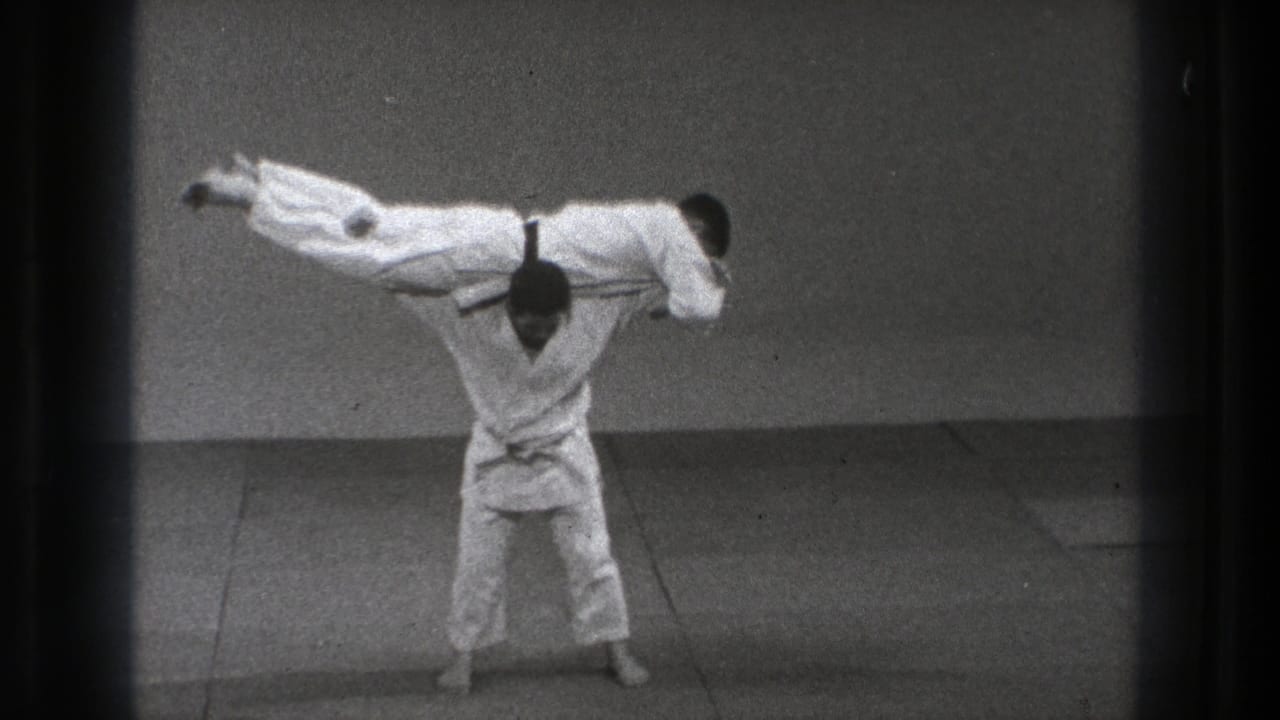 Tokyo 1971 8mm frame showing two adult men in white gi during a martial arts throw, with one practitioner lifted horizontally over the other.