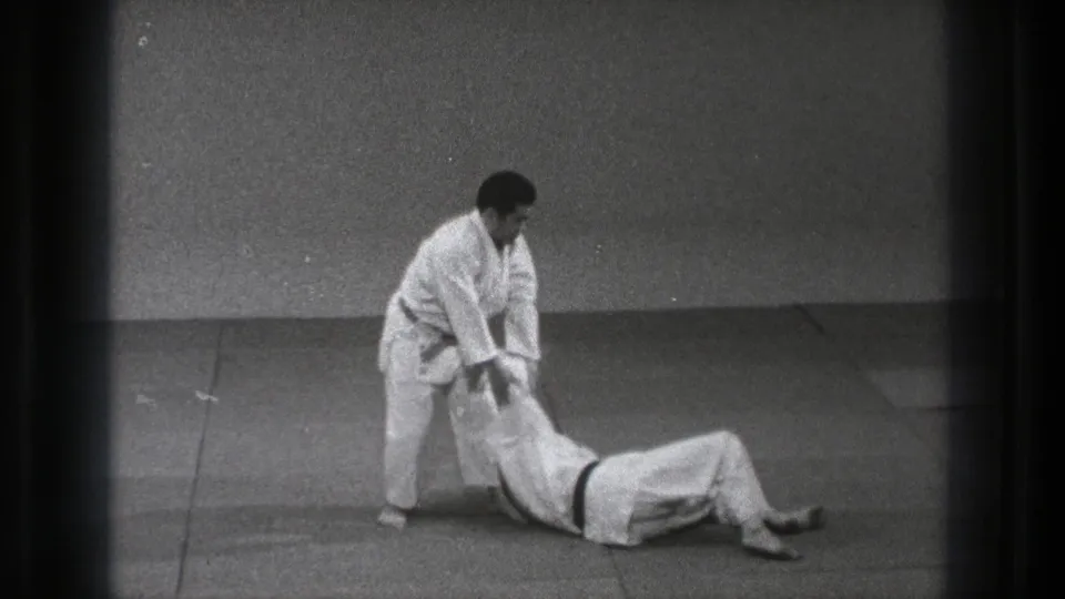Tokyo 1971 8mm frame showing the landing phase of a martial arts throw, with one man standing and the other on his back on the mat.
