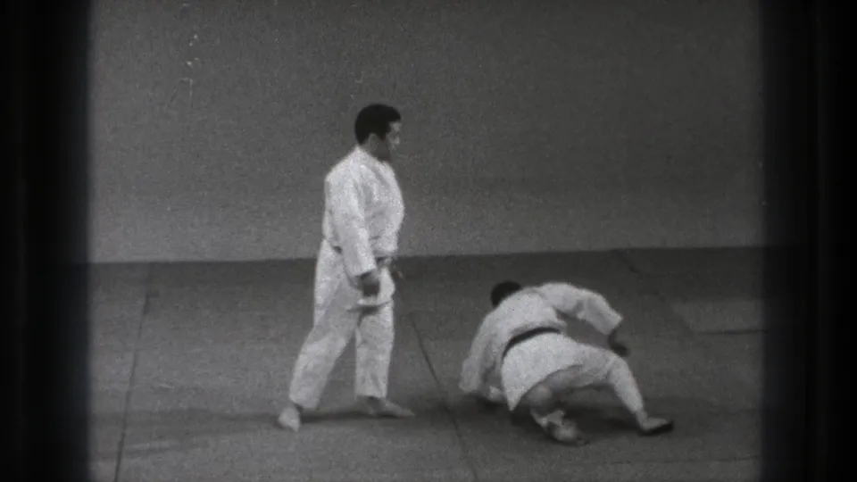 Tokyo 1971 8mm frame showing the aftermath of the throw, with one practitioner standing and the other recovering on the mat.