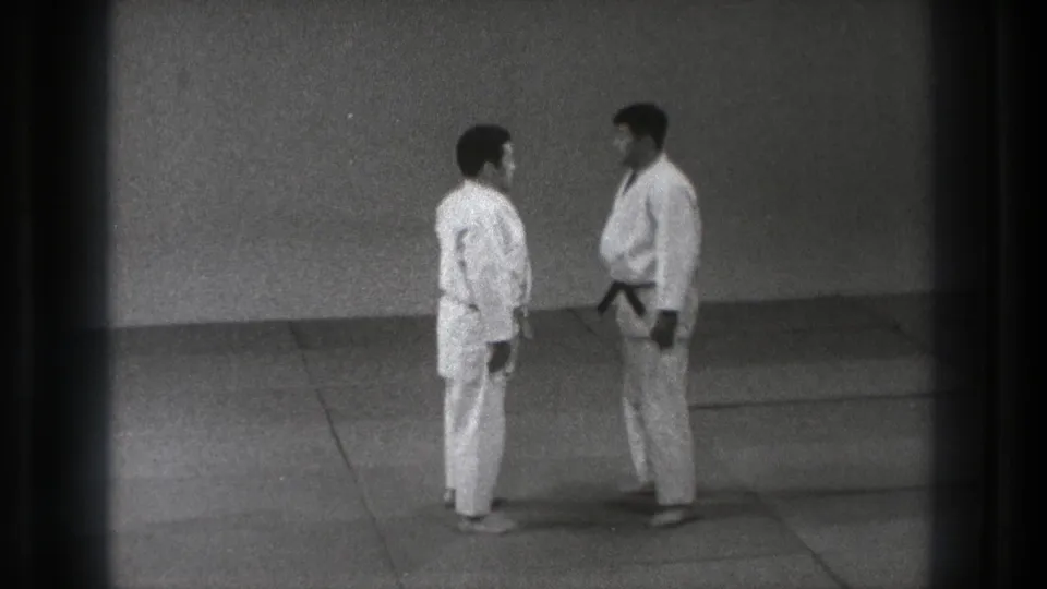 1971 Tokyo dojo frame showing two judo practitioners in gi standing close on the mat before a demonstration grip.