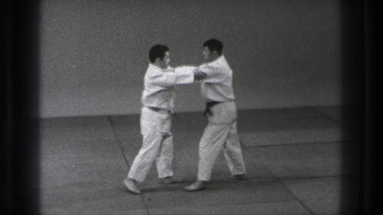 1971 Tokyo judo practice frame showing two gi-clad adults gripping sleeves or jackets during a controlled technique.