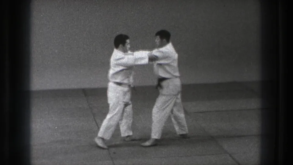 1971 Tokyo judo practice frame showing two gi-clad adults gripping sleeves or jackets during a controlled technique.