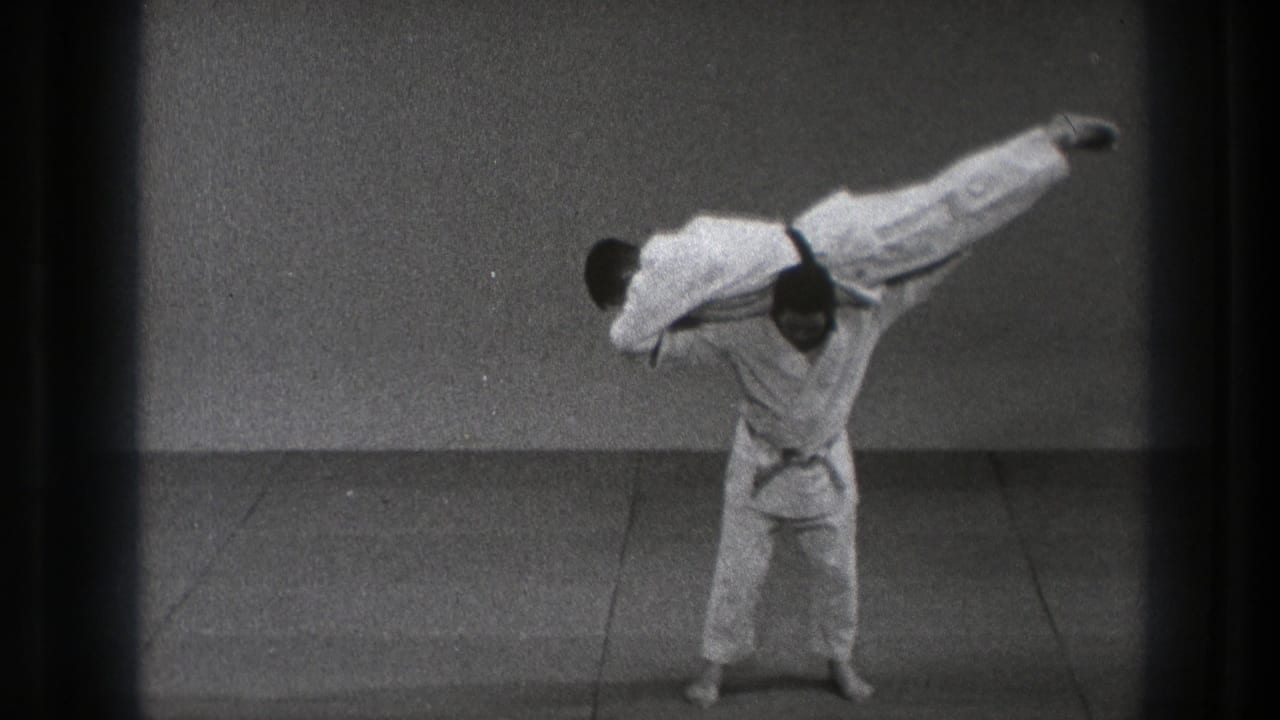 One man lifts another horizontally across his shoulders during a controlled judo throw demonstration in supported 1971 Tokyo footage.