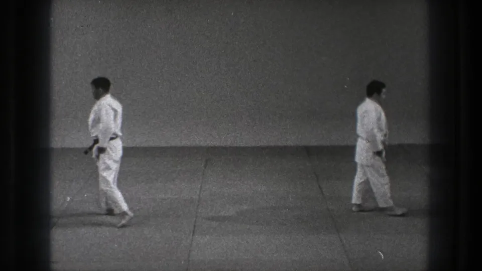 Two adult martial arts practitioners in white gi uniforms stand separated on a plain indoor floor in Tokyo, 1971.