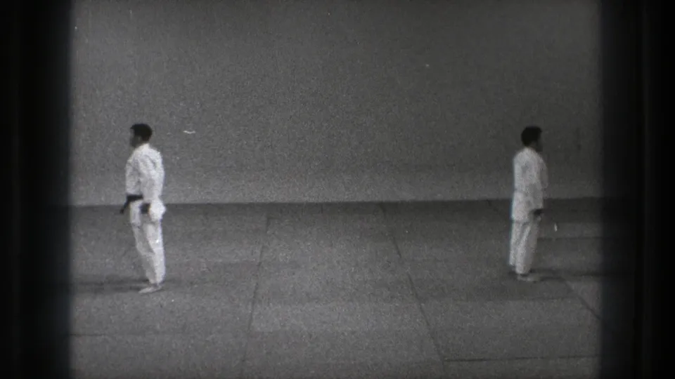 Two adult practitioners in white gi uniforms stand apart on a simple indoor floor in the Tokyo martial arts scene.