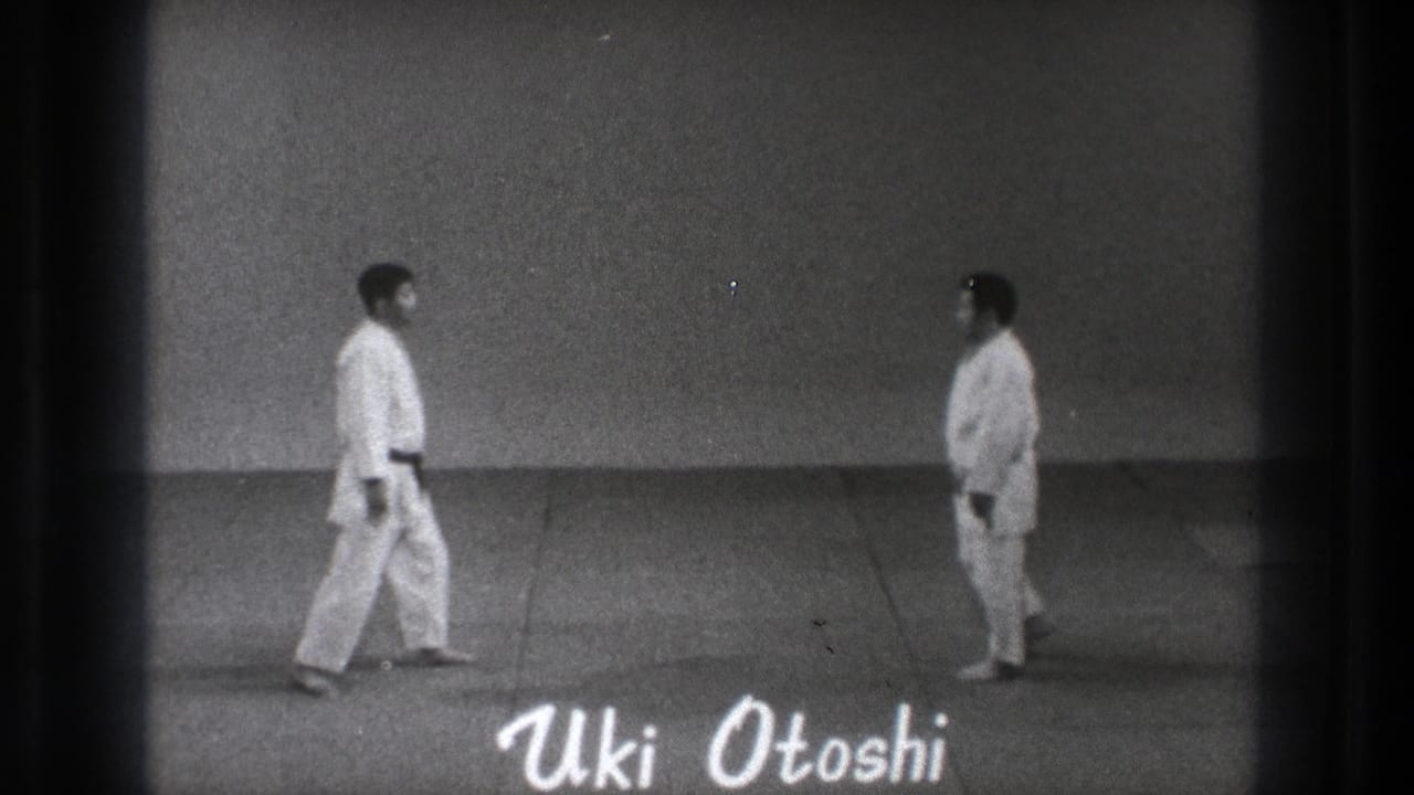 Two men in white judo uniforms stand apart on a mat with handwritten text reading Uki Otoshi.