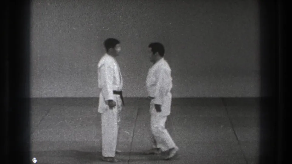 The two judoka stand nearly face to face on the dojo mat, holding a formal pause before contact or instruction.