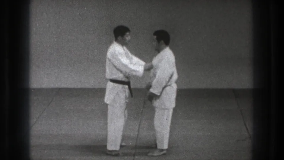 In the dojo practice sequence, one judoka reaches to the other's upper chest or lapel area as they begin a controlled judo movement.