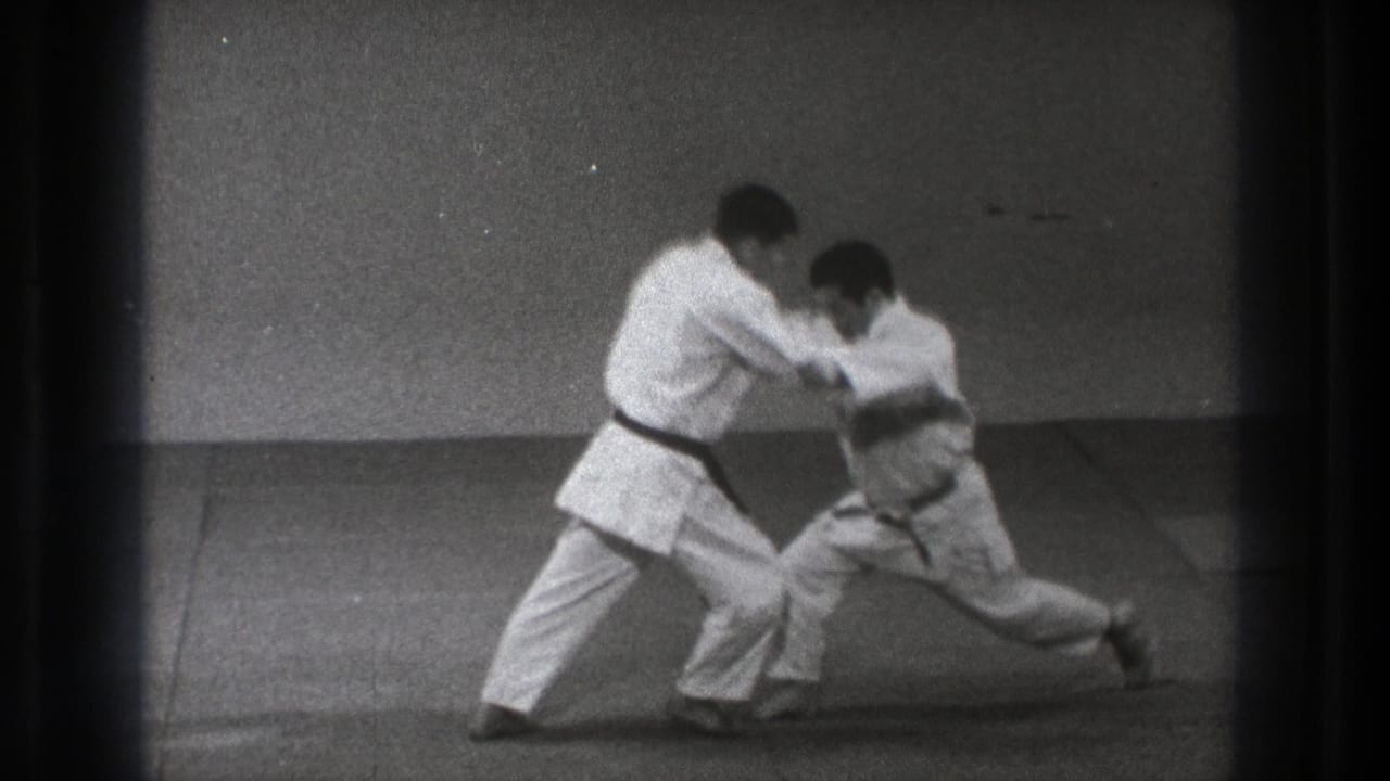 In the 1971 Tokyo martial arts clip, one man drops into a low stance as his partner controls the upper body during the technique.
