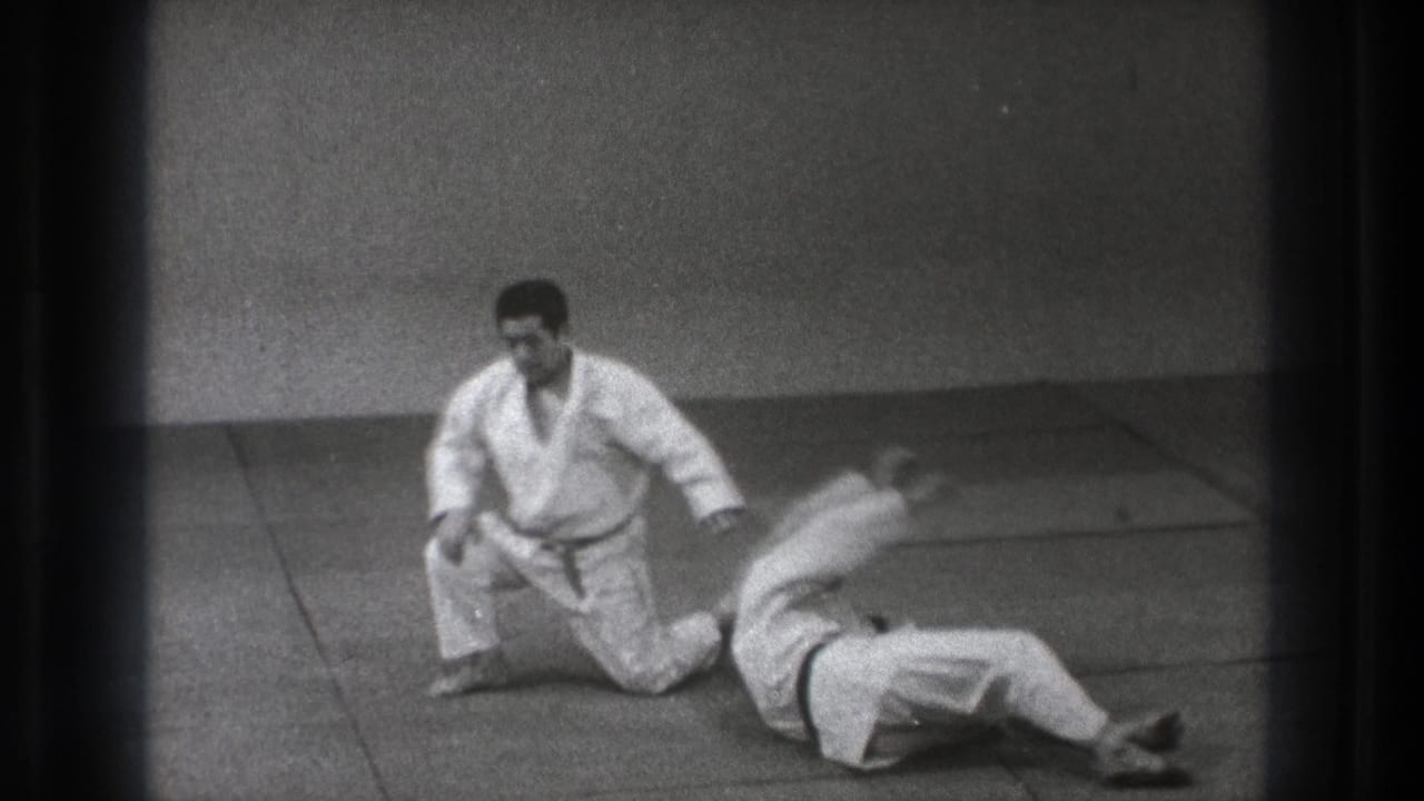After the throw, one judoka kneels upright while his partner lies on the mat in a simple indoor Tokyo practice space.