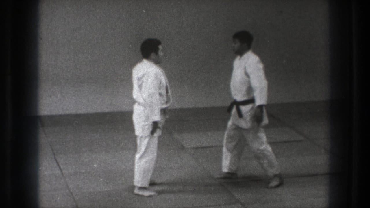 Two adult martial artists in white uniforms face each other on padded mats during a 1971 Tokyo practice sequence.