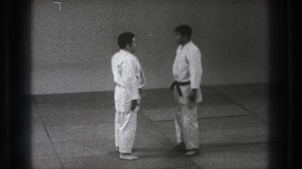In the closing frame, two martial artists stand close on the mat, appearing to complete the respectful exchange after sparring.