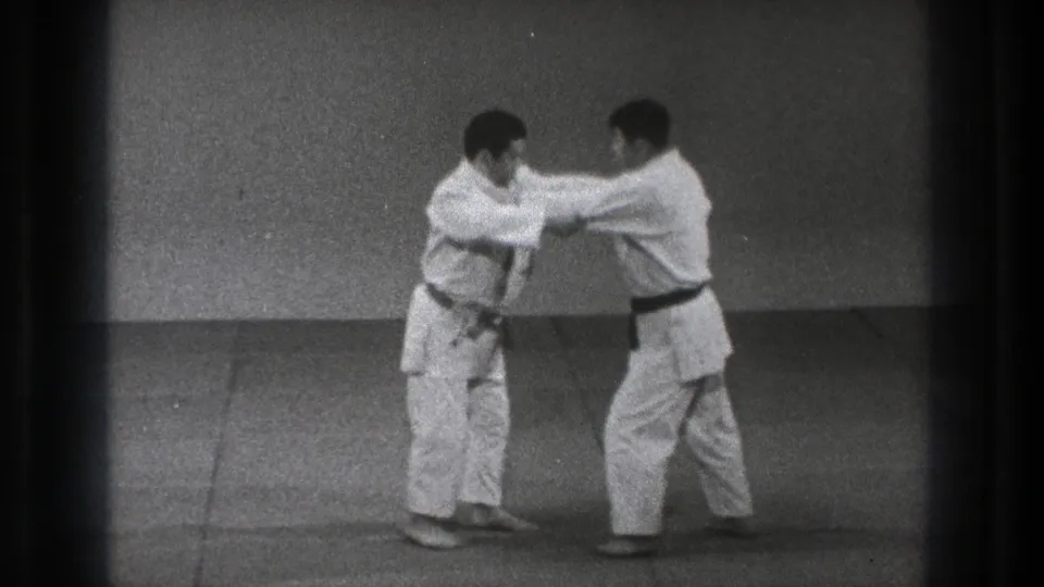 The practitioners close distance during the karate or grappling drill, with both men leaning into the exchange on the mat.