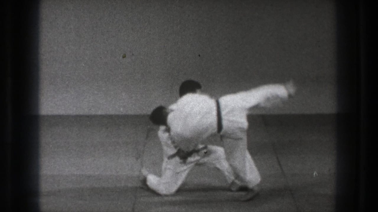 In 1971 Tokyo footage, one martial artist grips another while kneeling on a padded mat during a throw demonstration.