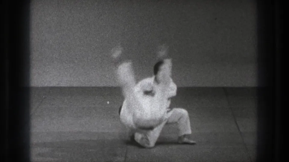 The throw reaches mid-motion as the training partner is lifted and rotated over the kneeling martial artist on the mat.