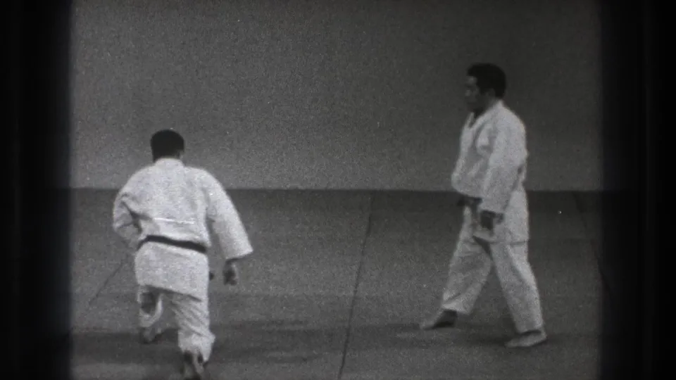 A 1971 Tokyo judo demonstration shows one practitioner rising or advancing from a low stance as the other waits on the mat.