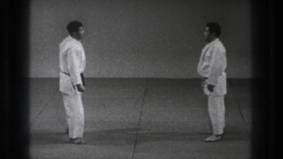 Two adult judo practitioners in white judogi stand facing each other in a simple Tokyo dojo setting from the supplied 1971 clip.
