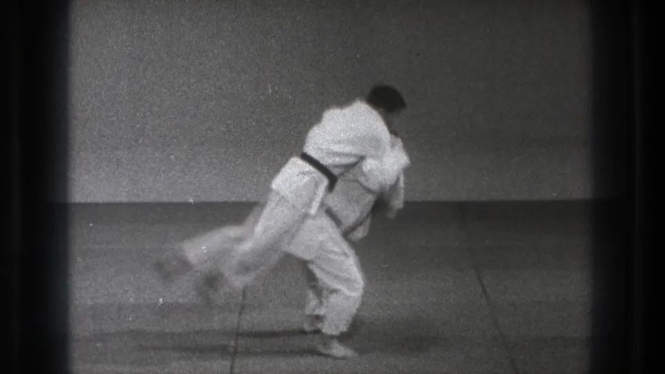 During the Tokyo martial arts demonstration, one man in a white gi is lifted and tipped across the black-belt practitioner's body.