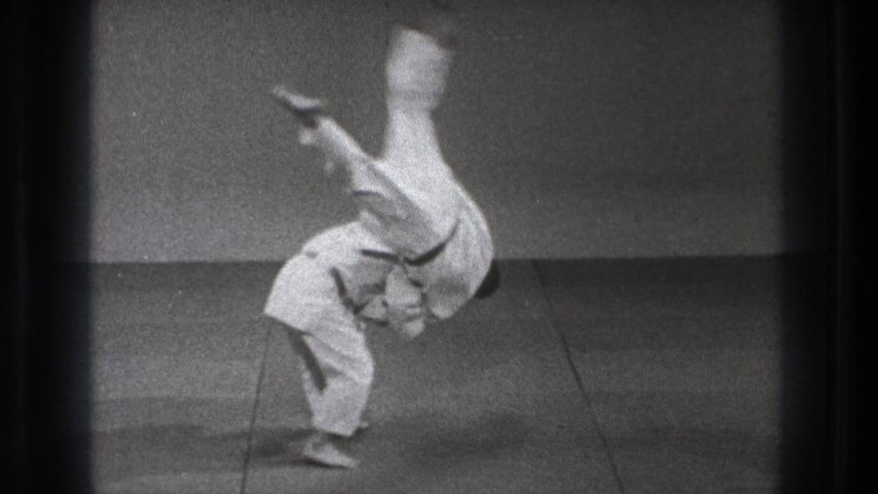Two men in gi perform a karate throw on an indoor mat.