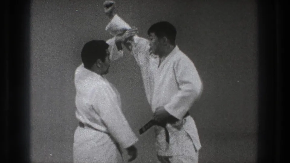 A closer 1971 Tokyo frame shows two karate practitioners in gi demonstrating hand and arm positioning during a drill.