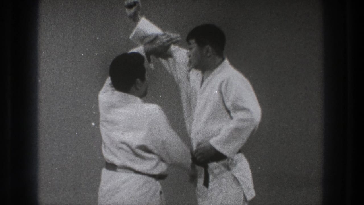 Two men in white martial arts uniforms begin a throwing technique indoors.