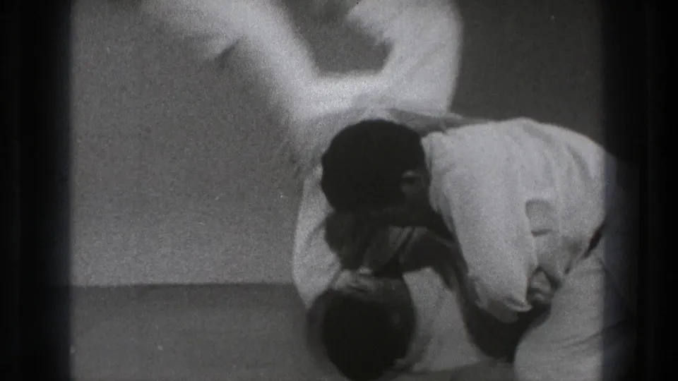 One adult man is flipped across the other practitioner's back during the final phase of the indoor martial arts demonstration.