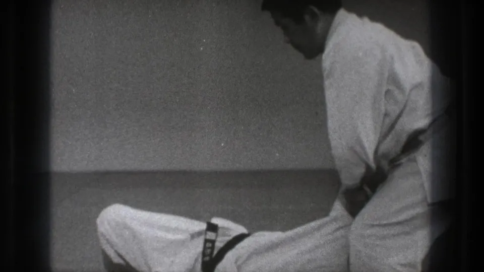 In the supplied Tokyo 1971 context, two karate practitioners in white gi appear on a mat during preparation or close-contact practice.