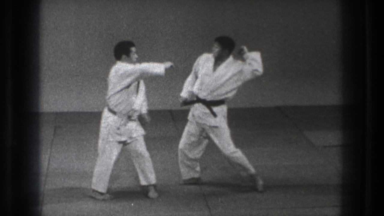 In Tokyo 1971 footage, two karate practitioners in white gi stand in a defensive exchange on a plain indoor mat.