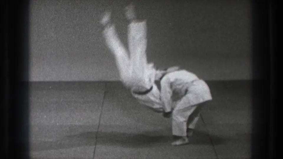 The throw continues as one martial artist rotates downward while the other stays bent and balanced on the dojo mat.