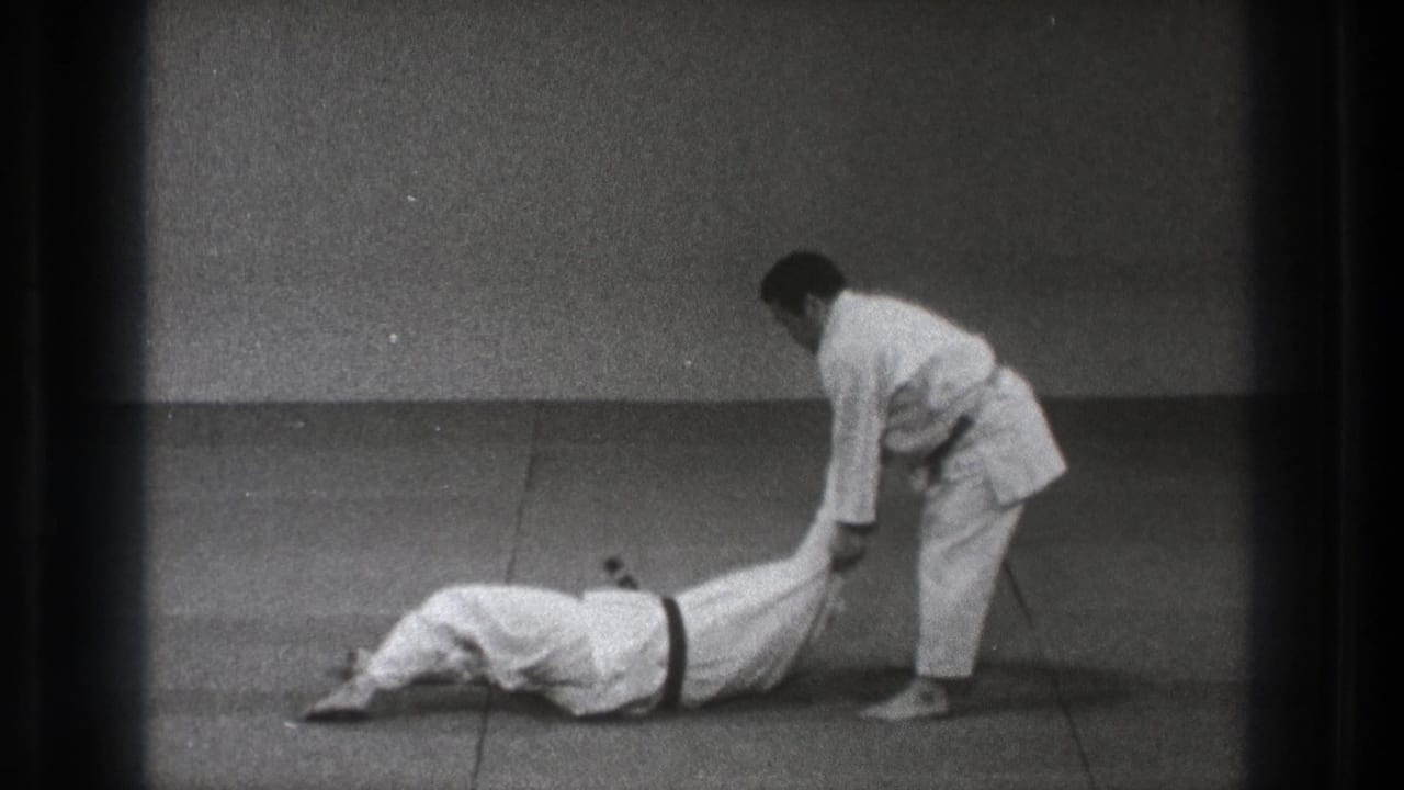 Two men in white gi practice a throw on a tatami mat.
