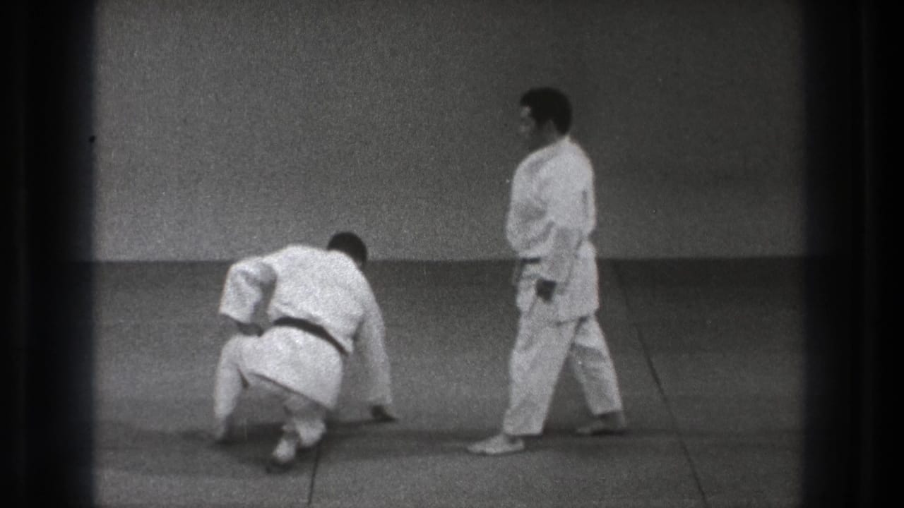 After the throw sequence, one man rises from the tatami while the other walks past in the 1971 Tokyo martial arts footage.