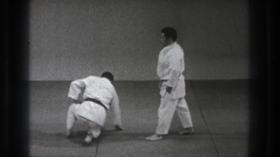 After the throw sequence, one man rises from the tatami while the other walks past in the 1971 Tokyo martial arts footage.