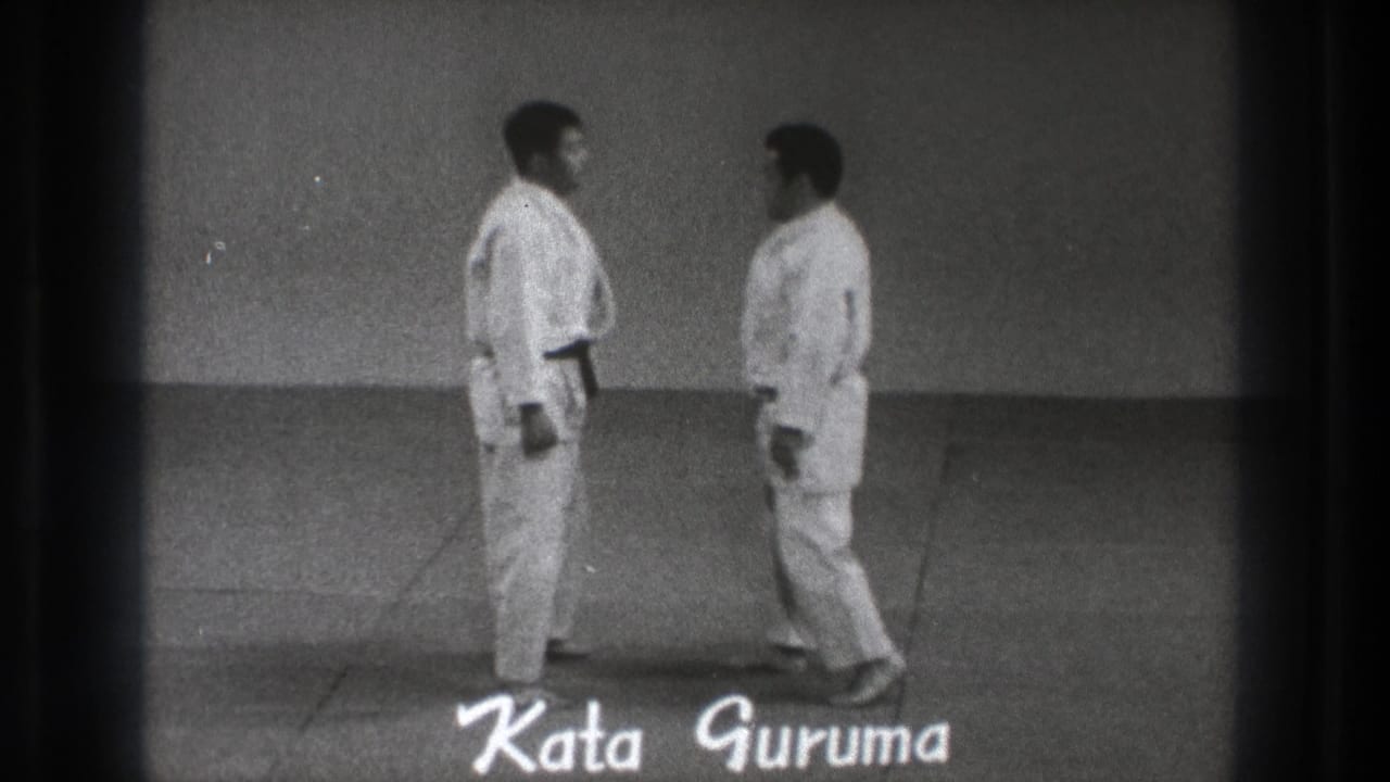 Two adult karate practitioners in white gi face each other as the handwritten title Kata Guruma appears over the 1971 Tokyo frame.