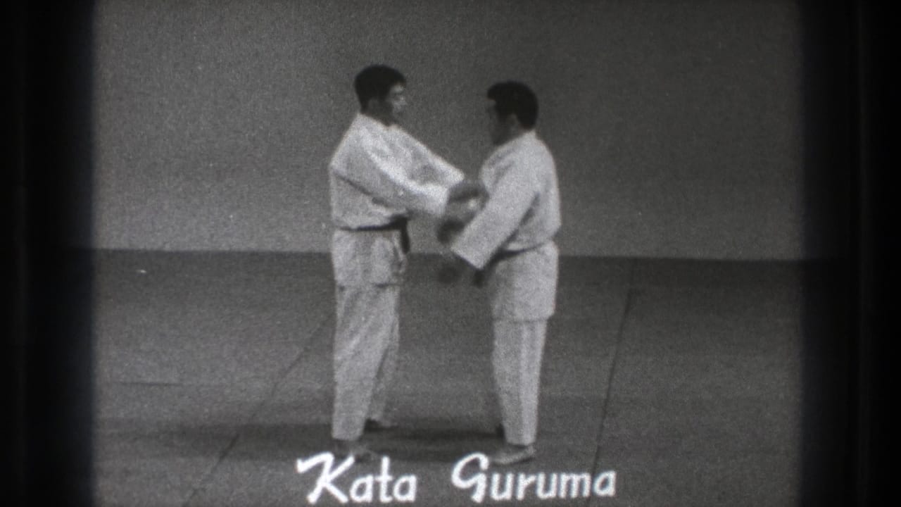 In the Tokyo karate demonstration, one adult man in a gi grips the other at close range during the Kata Guruma movement.